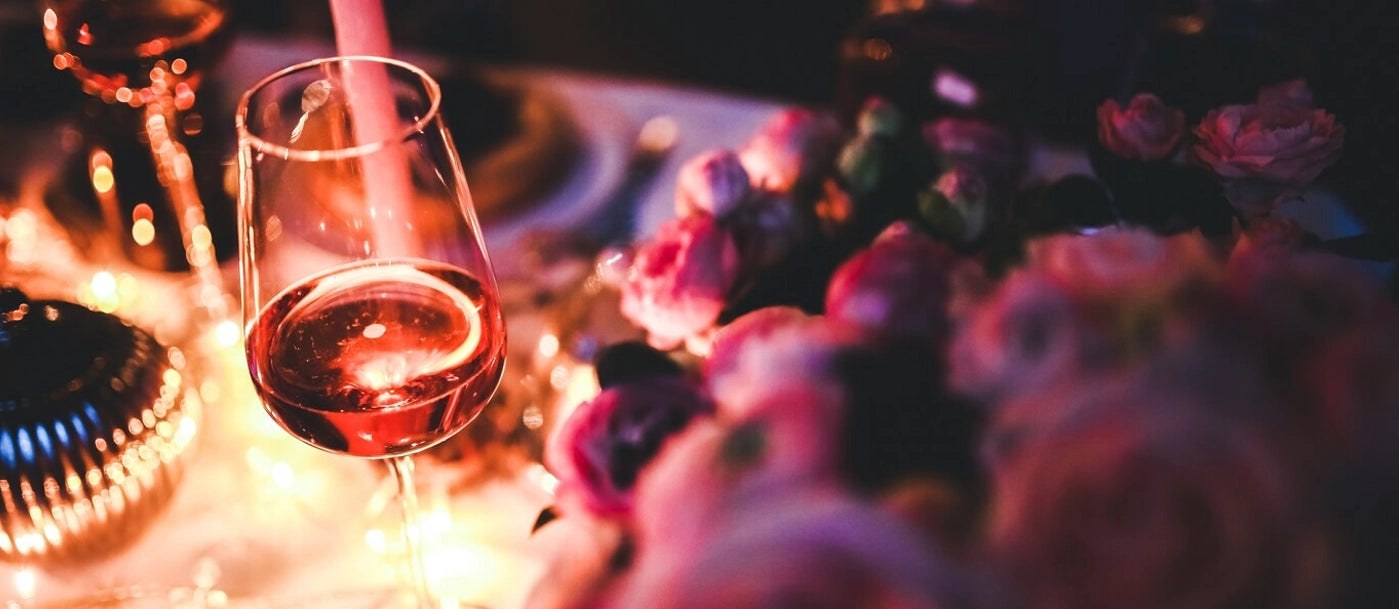 Elegant wine glass with rosé wine, surrounded by soft candlelight and delicate floral arrangements, creating a luxurious and romantic ambiance.